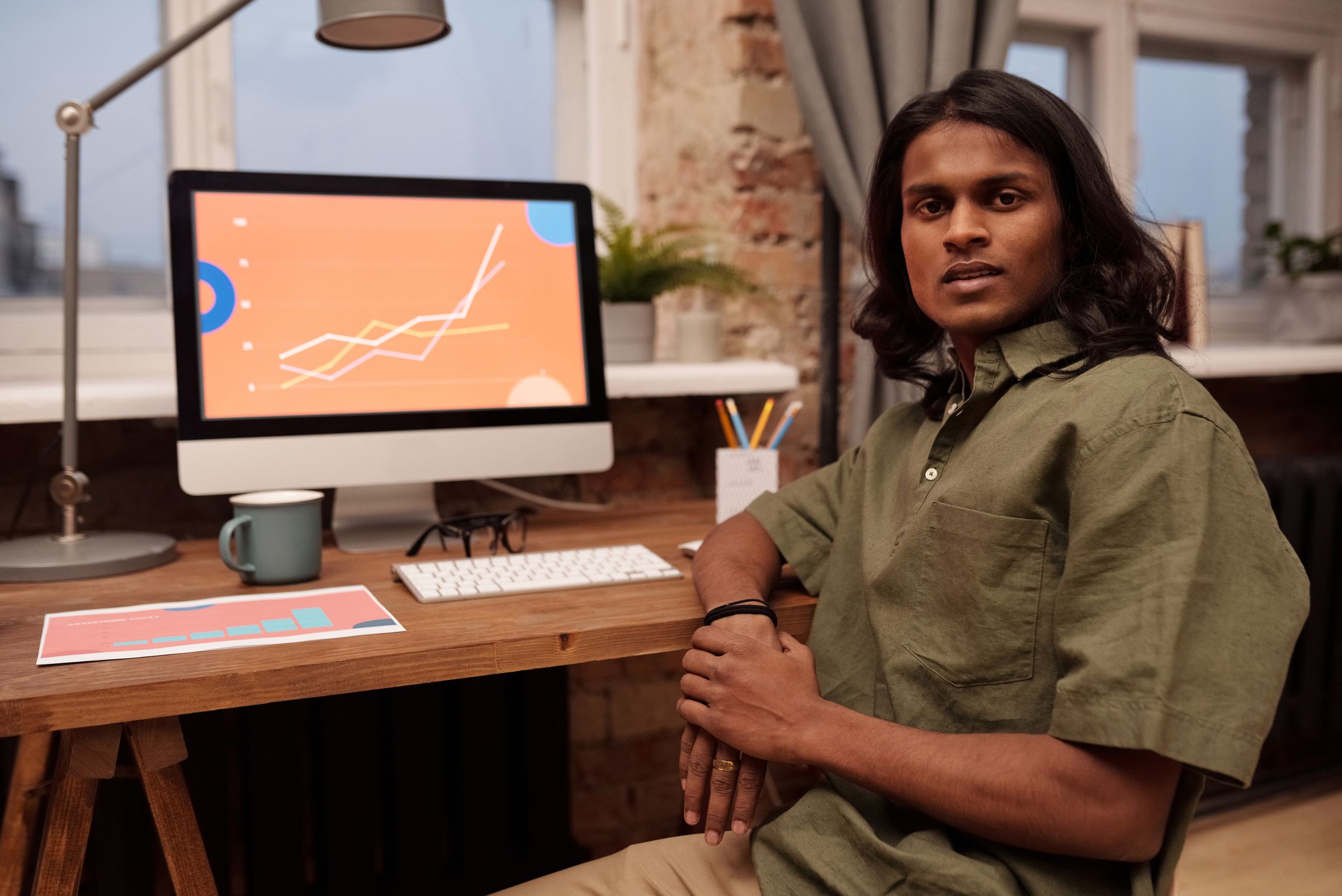 A young designer at his desk, a graphic on the screen behind him