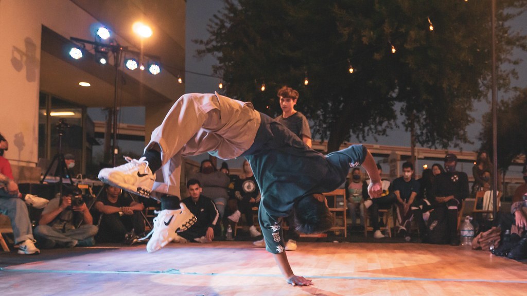 A breakdancer in a freeze at a jam, with the crowd seated around the circle
