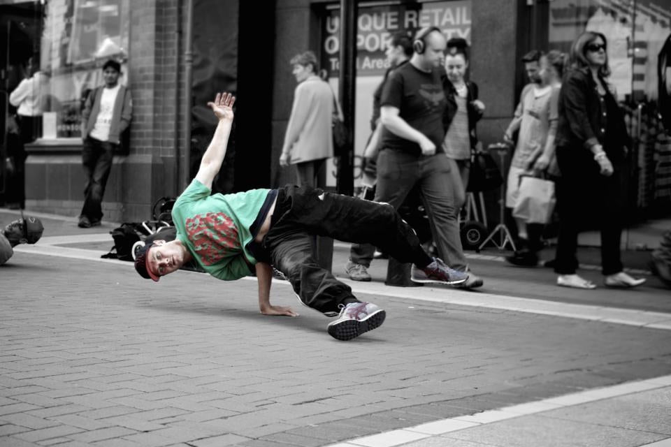 A breakdancer mid-move on a street, with a crowd watching